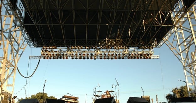 View from beneath a stage roof structure showing the scale of the roof grid, lighting truss, and rigging system.