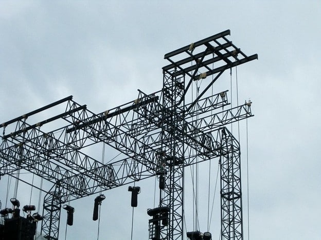 Complex stage rigging overhead showing multiple suspended lighting fixtures, truss spans, and hanging cable runs.